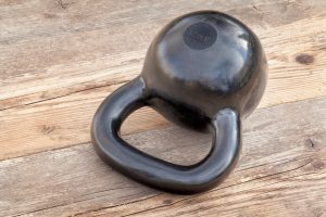 black 35 lb kettlebell for weight training on wood grunge deck, oudoors with sky reflections